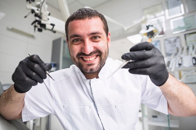 Primo piano di un dentista maschio felice che tiene gli strumenti dentali