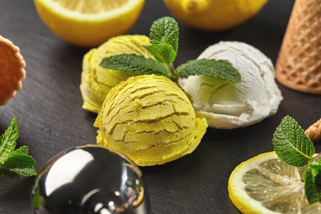 Primo piano di un gelato al limone e cremoso naturale fresco decorato con menta e servito su un'ardesia di pietra scura su sfondo nero. Lo scoop lucido si trova nelle vicinanze.