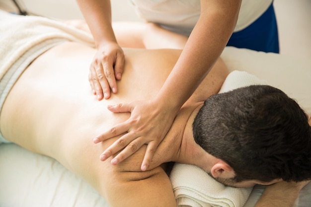 Primo piano di un giovane e delle mani di un terapista che danno un massaggio alla schiena in una clinica termale