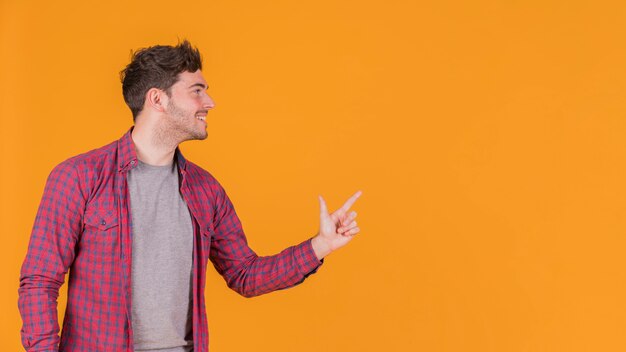 Primo piano di un giovane uomo che punta il dito contro qualcosa contro uno sfondo arancione