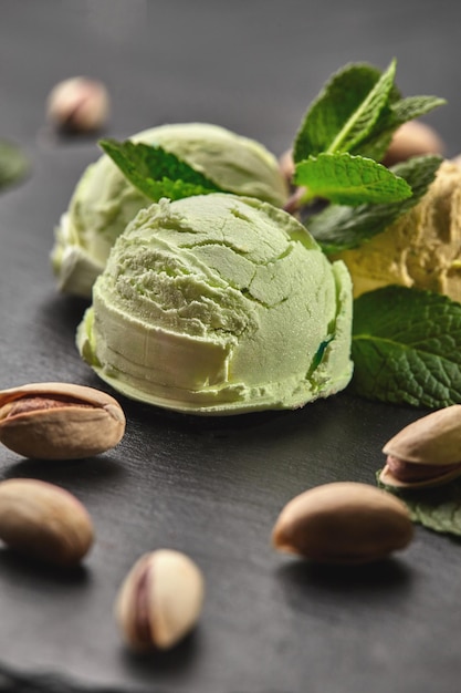 Primo piano di un gustoso gelato al pistacchio decorato con menta, pistacchi sparsi si trovano nelle vicinanze, servito su una pietra di ardesia su uno sfondo nero.