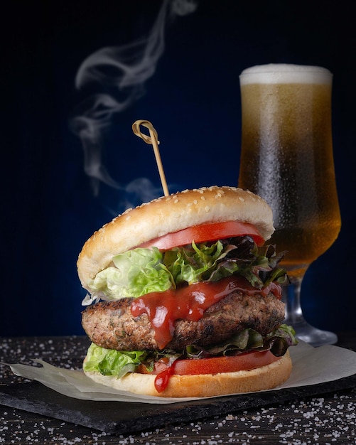 Primo piano di un hamburger caldo con una birra fredda sul tavolo su uno sfondo blu scuro