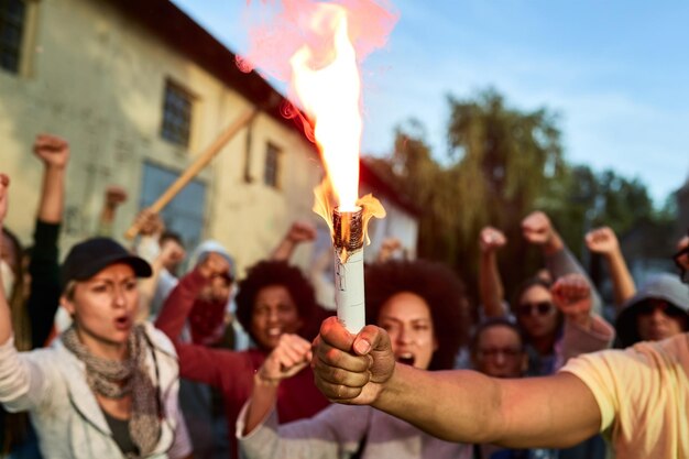 Primo piano di un manifestante che tiene in mano una torcia infiammata mentre la folla di persone grida in sottofondo