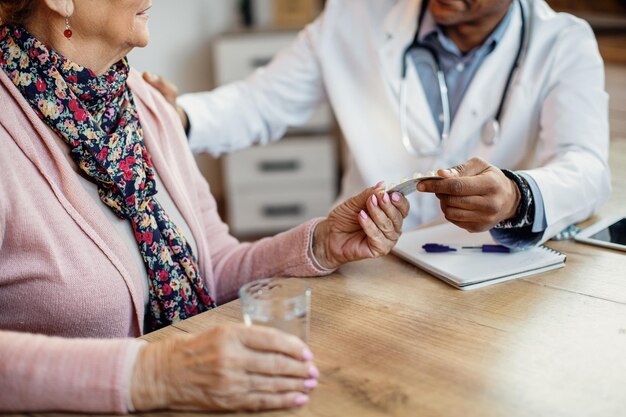 Primo piano di un medico che dà le pillole alla donna anziana durante la visita domiciliare