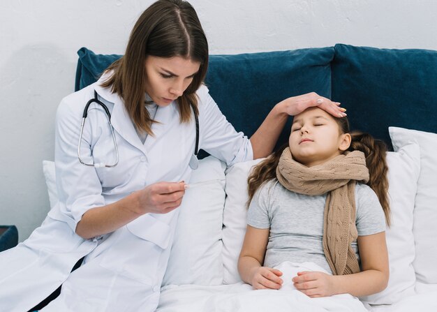 Primo piano di un medico femmina seduto vicino alla ragazza paziente guardando termometro