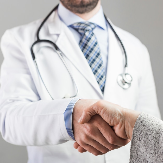 Primo piano di un medico maschio che stringe mano con il paziente contro fondo grigio