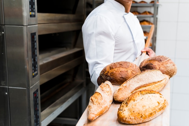 Primo piano di un panettiere maschio che tiene pane appena sfornato sulla pala di legno dal forno