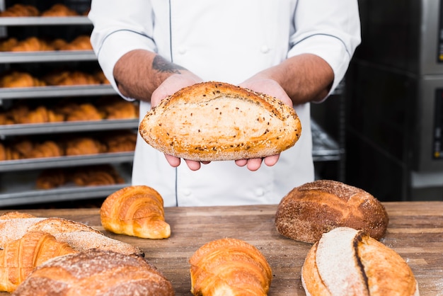 Primo piano di un panettiere maschio che tiene pane appena sfornato