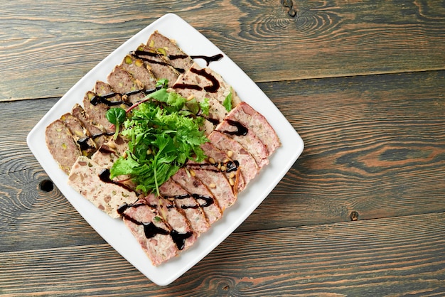 Primo piano di un piatto quadrato pieno di carne ripiena, decorato con foglie verdi e salsa di soia sul tavolo di legno.