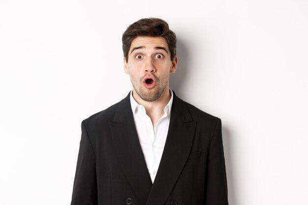 Primo piano di un uomo attraente in abito nero, che sembra sorpreso e impressionato dalla pubblicità, in piedi su sfondo bianco