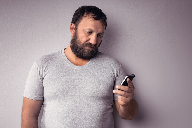 Primo piano di un uomo barbuto che indossa una camicia grigio chiaro con in mano uno smartphone su uno spazio grigio