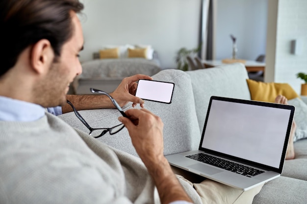 Primo piano di un uomo che legge un messaggio di testo sul telefono cellulare mentre lavora con il laptop a casa Copia spazio