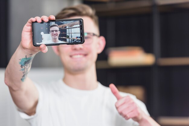 Primo piano di un uomo che prende selfie sul cellulare che mostra pollice sul segno