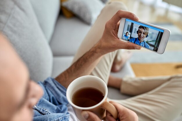 Primo piano di un uomo che usa lo smartphone e fa una videochiamata con un medico da casa