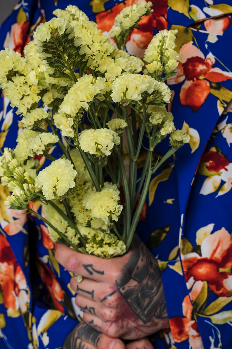 Foto gratuito primo piano di un uomo con il tatuaggio sulla sua mano che tiene il fiore di limonium in mano
