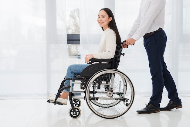 Primo piano di un uomo d&#39;affari che spinge la donna disabile che si siede sulla sedia a rotelle