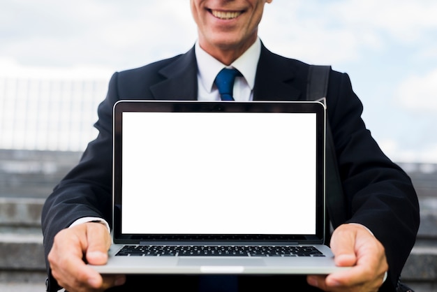 Primo piano di un uomo d&#39;affari maturo felice che mostra computer portatile con lo schermo bianco in bianco