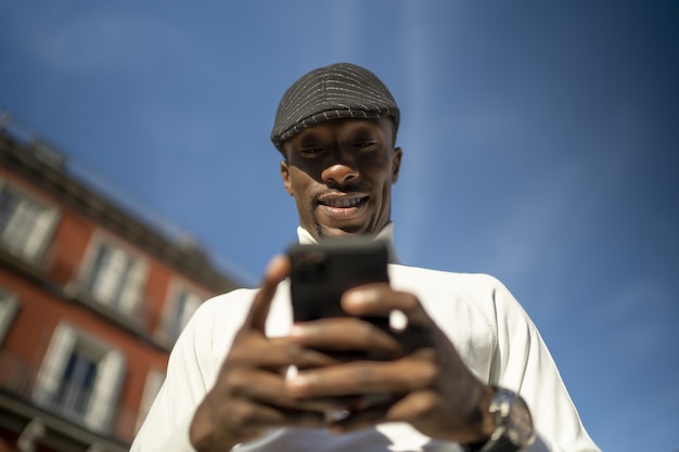 Primo piano di un uomo di colore che indossa un dolcevita e un cappello che guarda il suo telefono
