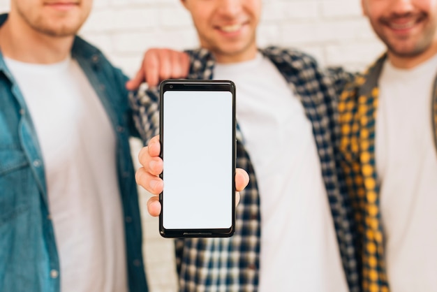 Primo piano di un uomo in piedi con i suoi due amici mostrando cellulare con display bianco