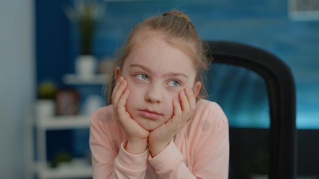 Primo piano di una bambina che si sente esausta e guarda il computer per una lezione di classe online. Ritratto di bambino che frequenta corsi scolastici da casa. Allievo stanco con l'istruzione a distanza