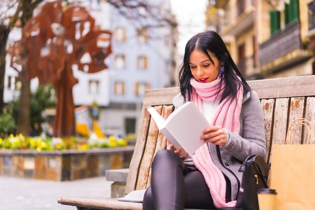 Primo piano di una bella donna caucasica seduta su una panchina e che legge un libro in un parco pubblico