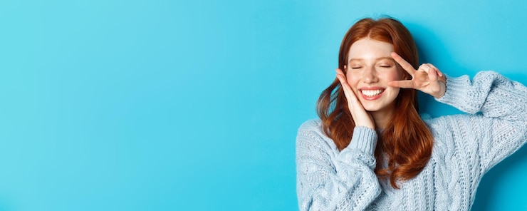 Foto gratuito primo piano di una bella ragazza sorridente con i capelli rossi che mostra il segno di pace kawaii in piedi con gli occhi chiusi