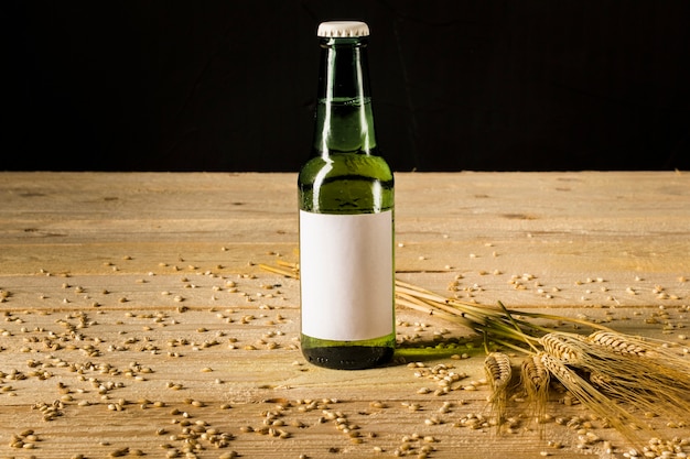 Primo piano di una bottiglia alcolica e spighe di grano sulla plancia di legno