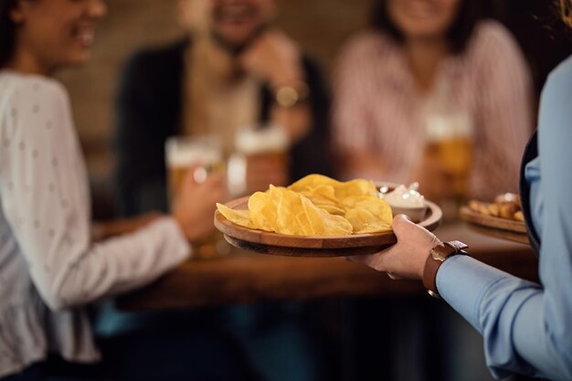 Primo piano di una cameriera irriconoscibile che serve tortilla chips agli ospiti in una taverna