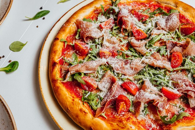 Primo piano di una deliziosa pizza al formaggio con prosciutto, pomodori e verdure su un piatto