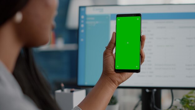 Primo piano di una donna africana che tiene in mano un telefono chroma key con schermo verde con display isolato