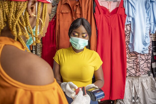 Primo piano di una donna africana con guanti in lattice e una maschera facciale che paga con carta di credito in un negozio