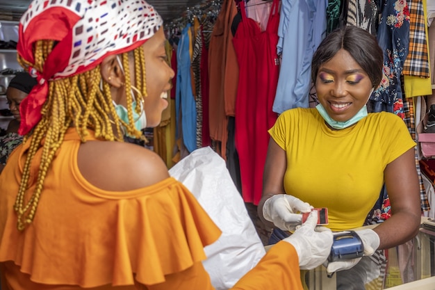 Primo piano di una donna africana con guanti in lattice e una maschera facciale che paga con una carta di credito in un negozio
