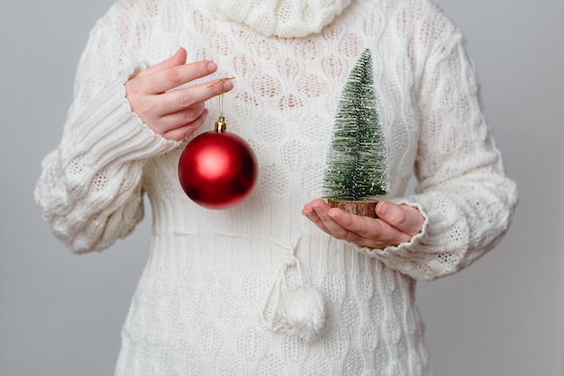 Primo piano di una donna bianca che tiene un minuscolo albero di Natale in uno e una palla rossa nell'altra