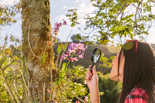 Primo piano di una donna che guarda fiore rosa attraverso la lente di ingrandimento