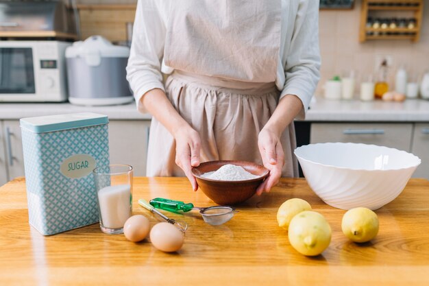 Primo piano di una donna che prepara torta in cucina con ingredienti sul tavolo