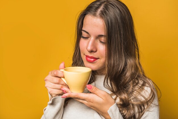 Primo piano di una donna che sente l&#39;odore del caffè dalla tazza gialla