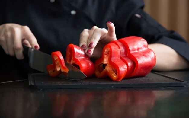 Primo piano di una donna che taglia peperone rosso sul tagliere con il coltello