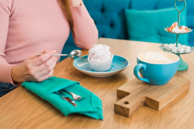 Primo piano di una donna con meringa e tazza di caffè sul tavolo di legno