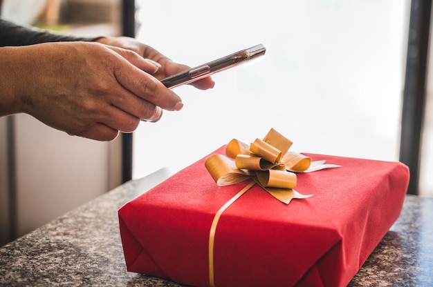 Primo piano di una donna con uno smartphone che cattura una foto di una confezione regalo rossa sul bancone