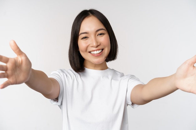 Primo piano di una donna coreana sorridente felice che raggiunge le mani che si abbracciano allungando le braccia per ricevere un caloroso benvenuto in piedi su sfondo bianco