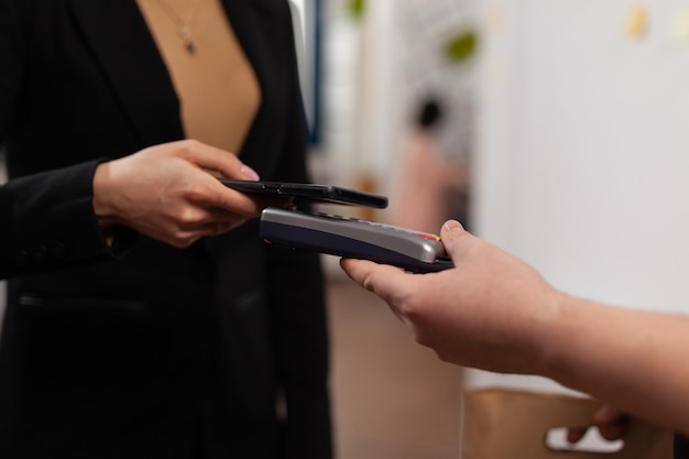 Primo piano di una donna d'affari che paga il ragazzo delle consegne dal servizio frood, utilizzando la tecnologia nfc dello smartphone