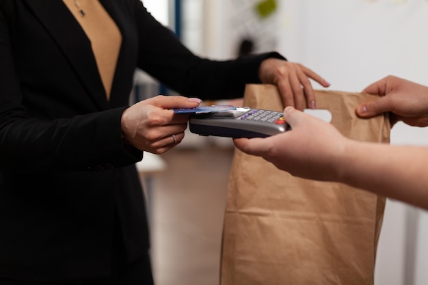 Primo piano di una donna d'affari in possesso di carta di credito pos, utilizzando la tecnologia senza contatto, pagando cibo da asporto dal corriere