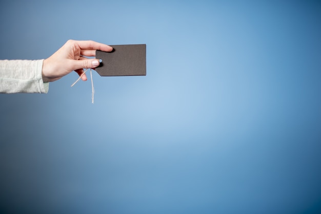 Primo piano di una donna in possesso di un tag vuoto con uno sfondo blu - ottimo per la scrittura di testo