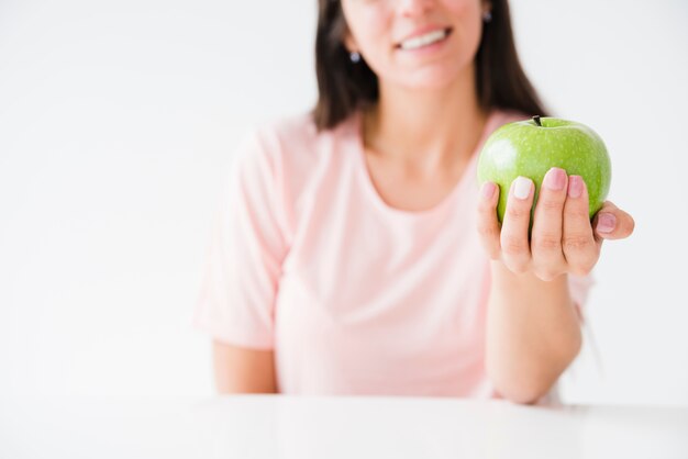 Primo piano di una donna sorridente che mostra mela verde in mano contro il contesto bianco