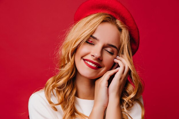 Primo piano di una donna sorridente e allegra in berretto rosso Signora francese spensierata con i capelli lunghi che si gode il servizio fotografico al coperto