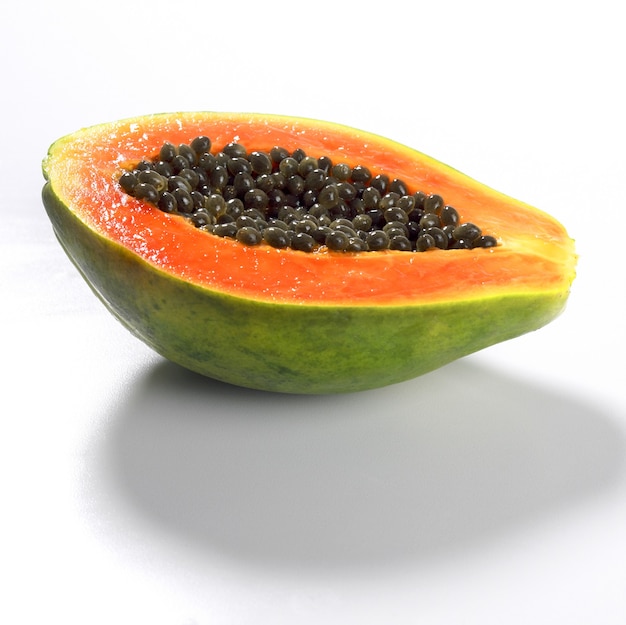 Primo piano di una frutta fresca della papaia tagliata a metà isolata su una superficie bianca