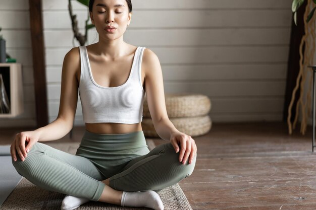 Primo piano di una giovane atleta asiatica di fitness a casa che fa allenamento sul tappetino meditando e stret...