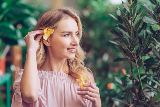 Primo piano di una giovane donna che pone il fiore giallo dietro il suo orecchio