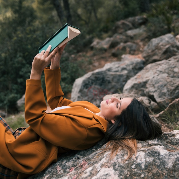 Primo piano di una giovane donna che si appoggia sulla roccia leggendo il libro