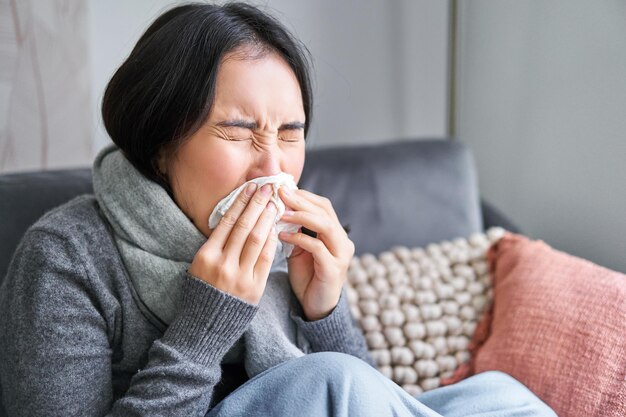 Primo piano di una giovane donna coreana che sta a casa con starnuti freddi in tovagliolo ha il naso che cola concetto di malattia salute e influenza